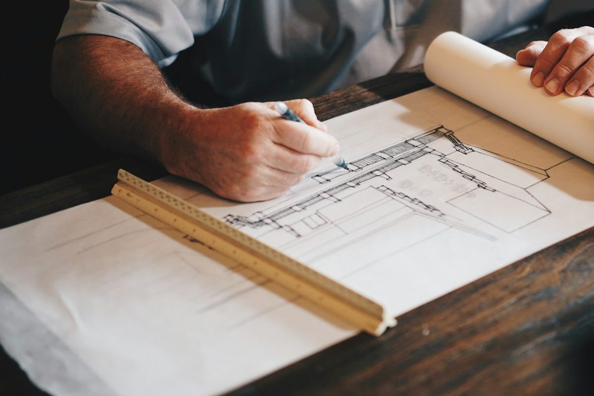 Hands drafting a technical plan with a ruler and pencil